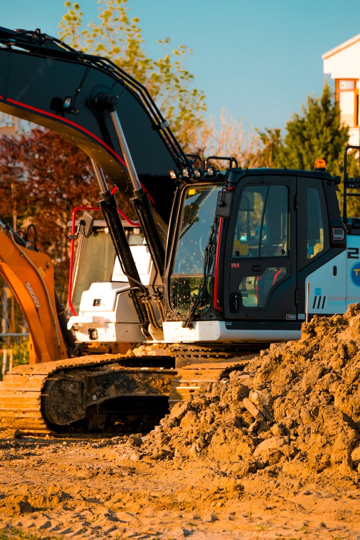 Excavator at a construction site with dirt piles and trees in background.