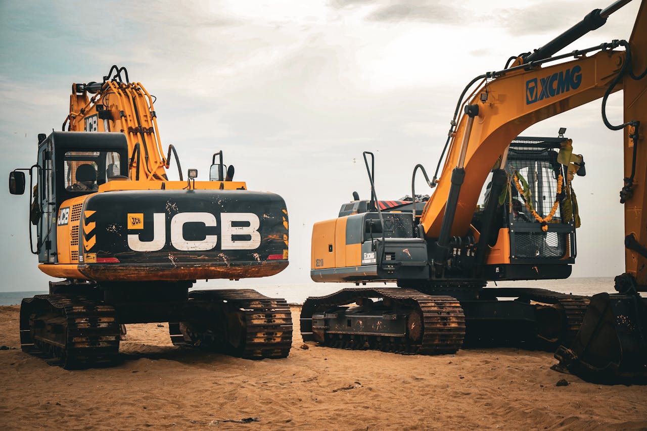 Two heavy excavators on a sandy beach, showcasing industrial construction machinery.
